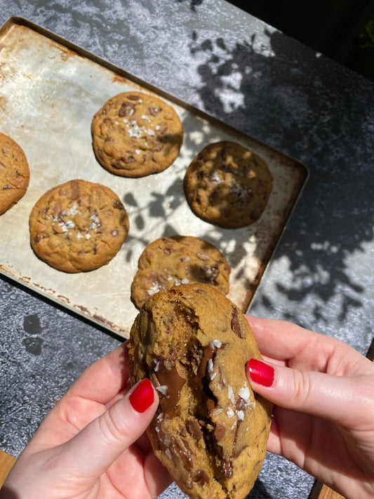 Hand breaking a Bikkie Haus Sydney chocolate chip cookie above a baking tray with more cookies