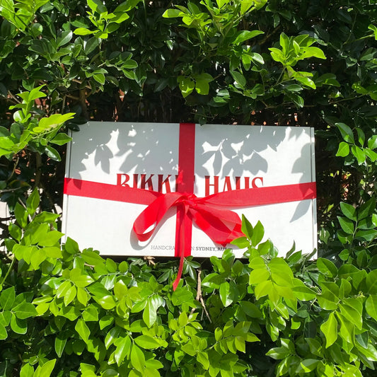 White Bikkie Haus Sydney cookie gift box with a red ribbon on green foliage